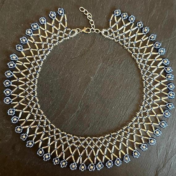 A lace collar necklace made from blue and silver beads lying on a grey slate.