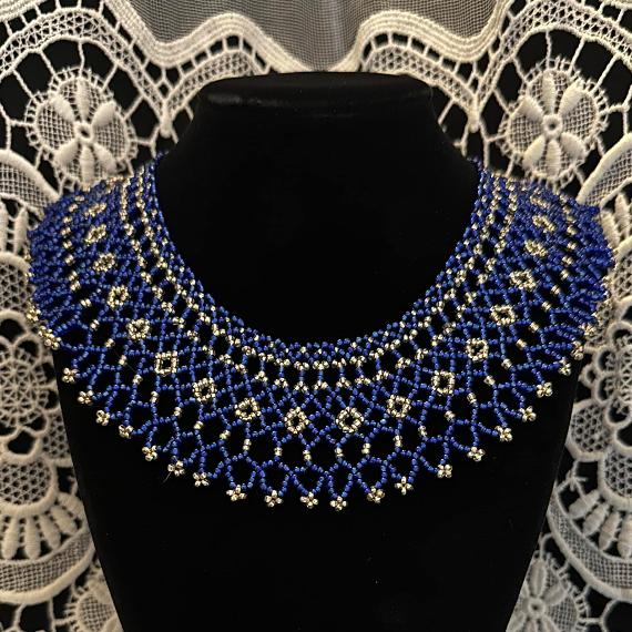 A photo of a blue and silver lace collar necklace on a velvet stand with a white lace background.