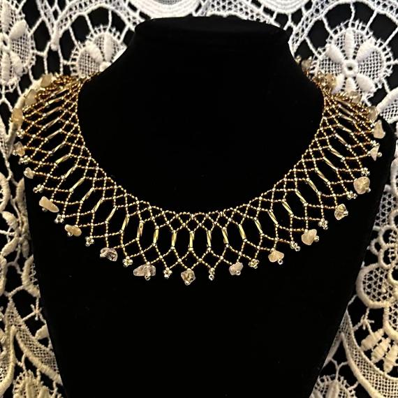 A lace collar necklace made from beads on a velvet stand.