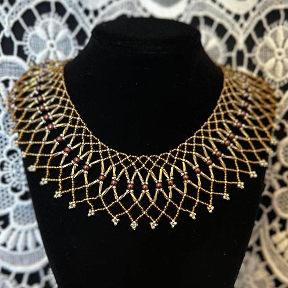 A photo of a beaded lace collar necklace on a velvet stand with a white lace background.