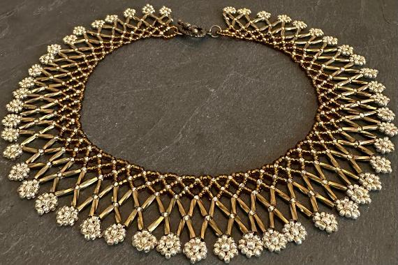 A bronze lace collar necklace made from beads lying on a grey slate.