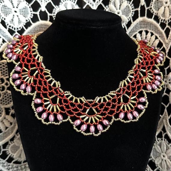 A photo of a red and gold lace collar necklace on a velvet stand with a white lace background.