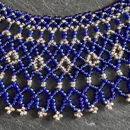 A close up photo of a blue and silver beaded collar necklace.