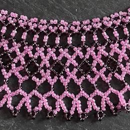 A close up view of a pink and grey beaded lace necklace.