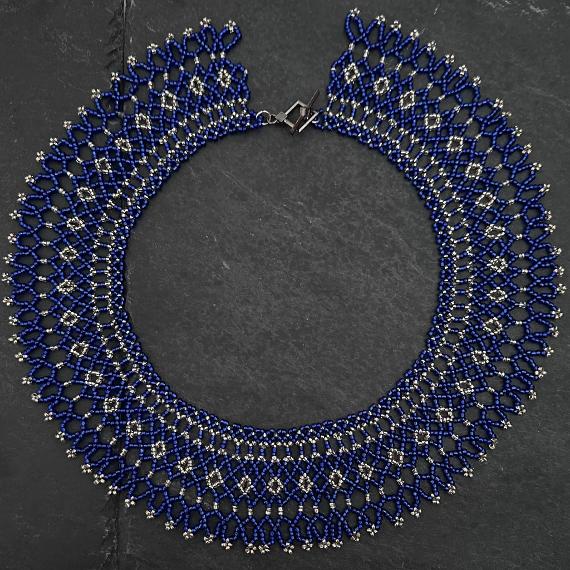 A lace collar necklace made from blue and silver beads lying on a grey slate.