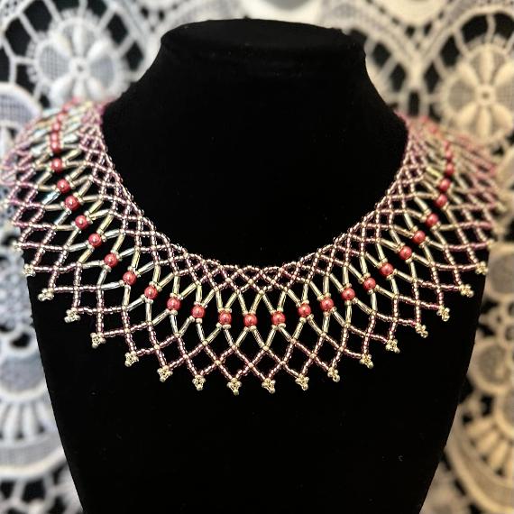 A pink lace collar necklace made from beads on a velvet stand.