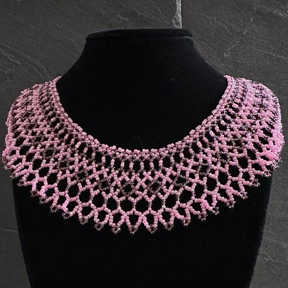 A pink lace collar necklace made from beads on a velvet stand.