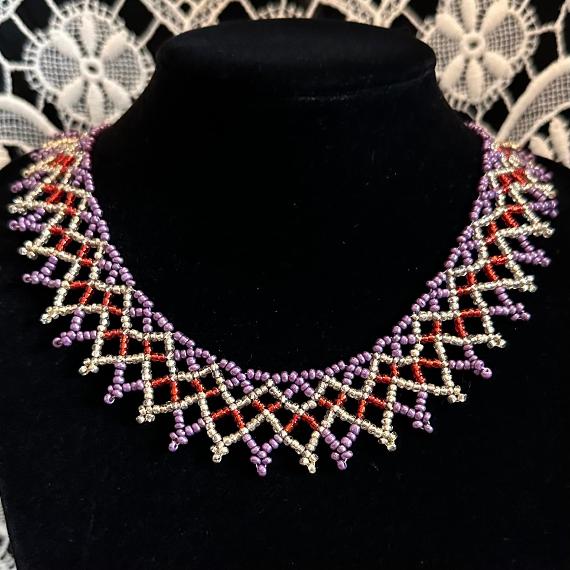 A photo of a beaded lace collar necklace on a velvet stand with a white lace background.