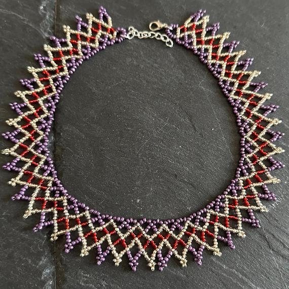 A lace collar necklace made from tiny beads lying on a grey slate.