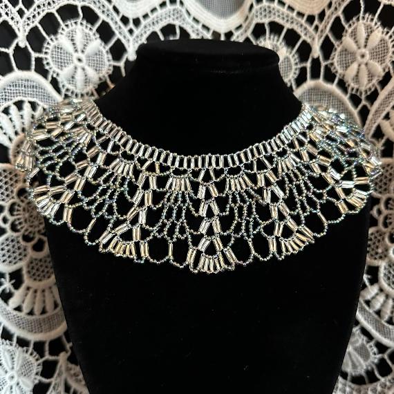 A photo of a lace collar necklace on a velvet stand with a white lace background.