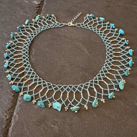 A lace collar necklace made from tiny beads lying on a grey slate.