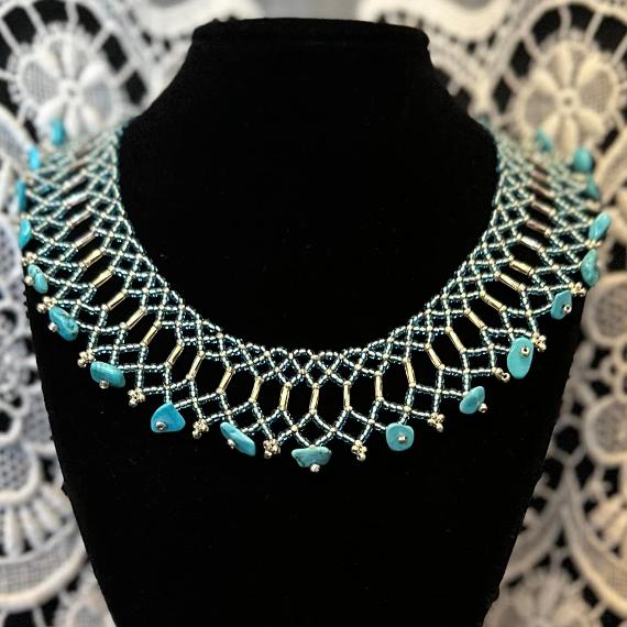 A photo of a beaded lace collar necklace on a velvet stand with a white lace background.